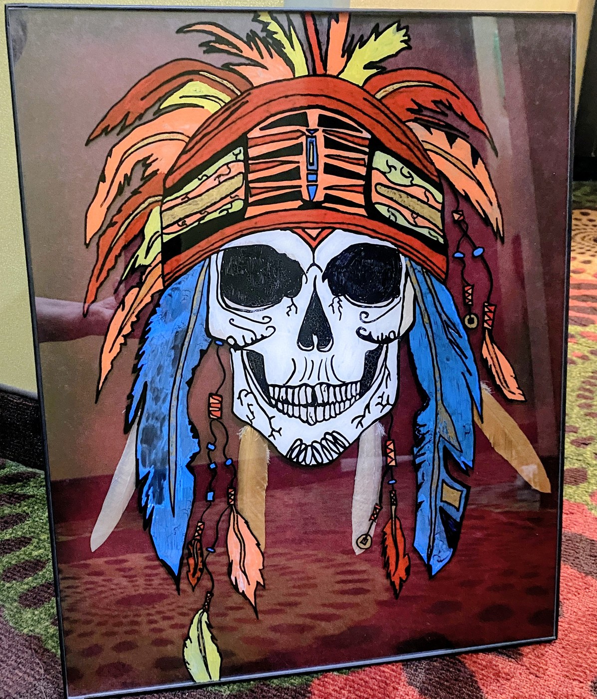 A skull crowned with a feathered headdress in orange, blue and gold
